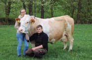 Benedikt Kappauf kniet neben Kuh auf Weide, Frau steht dahinter